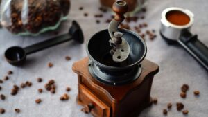An old hand grinder on a table surrounded by coffee beans.