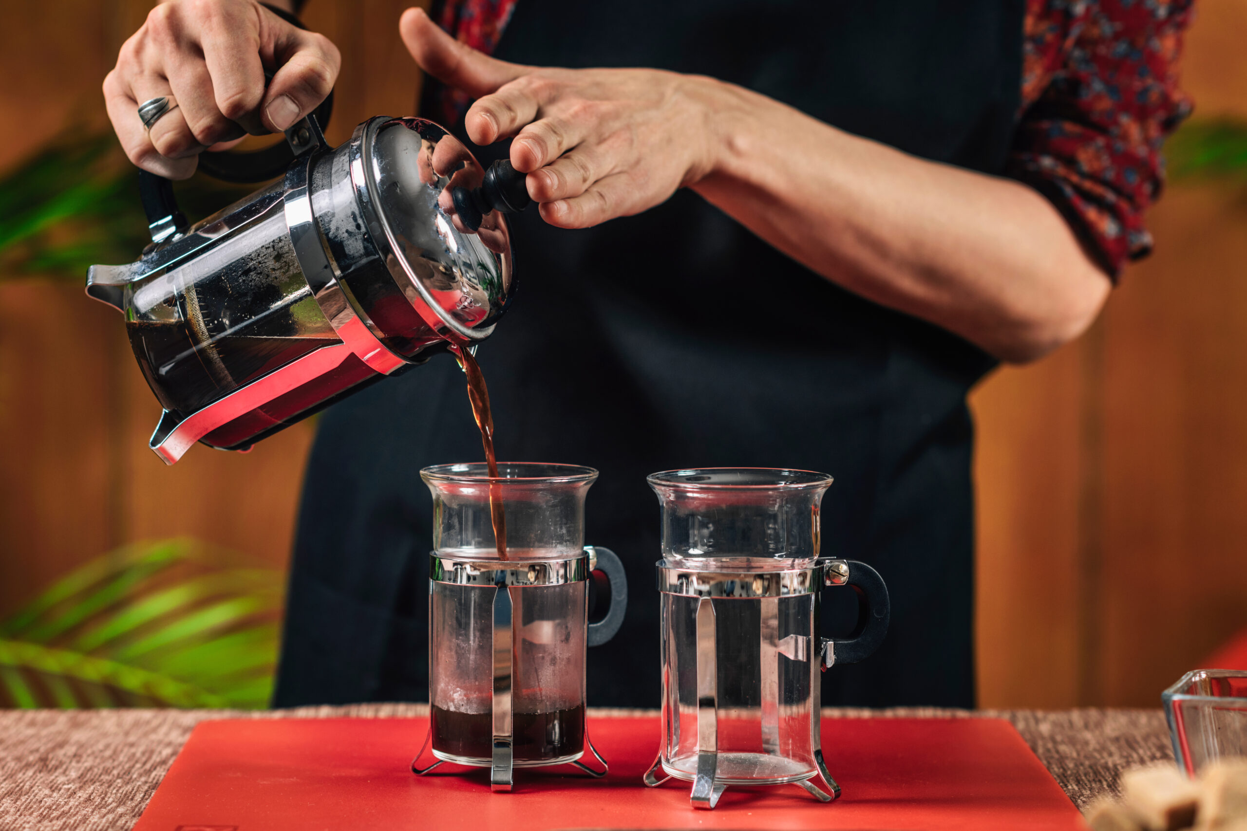 French Press Coffee. Barista Pouring French Press Coffee A barista pouring coffee from a large French press into two smaller French presses.