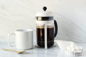 A white French press on a counter next to a white coffee mug.