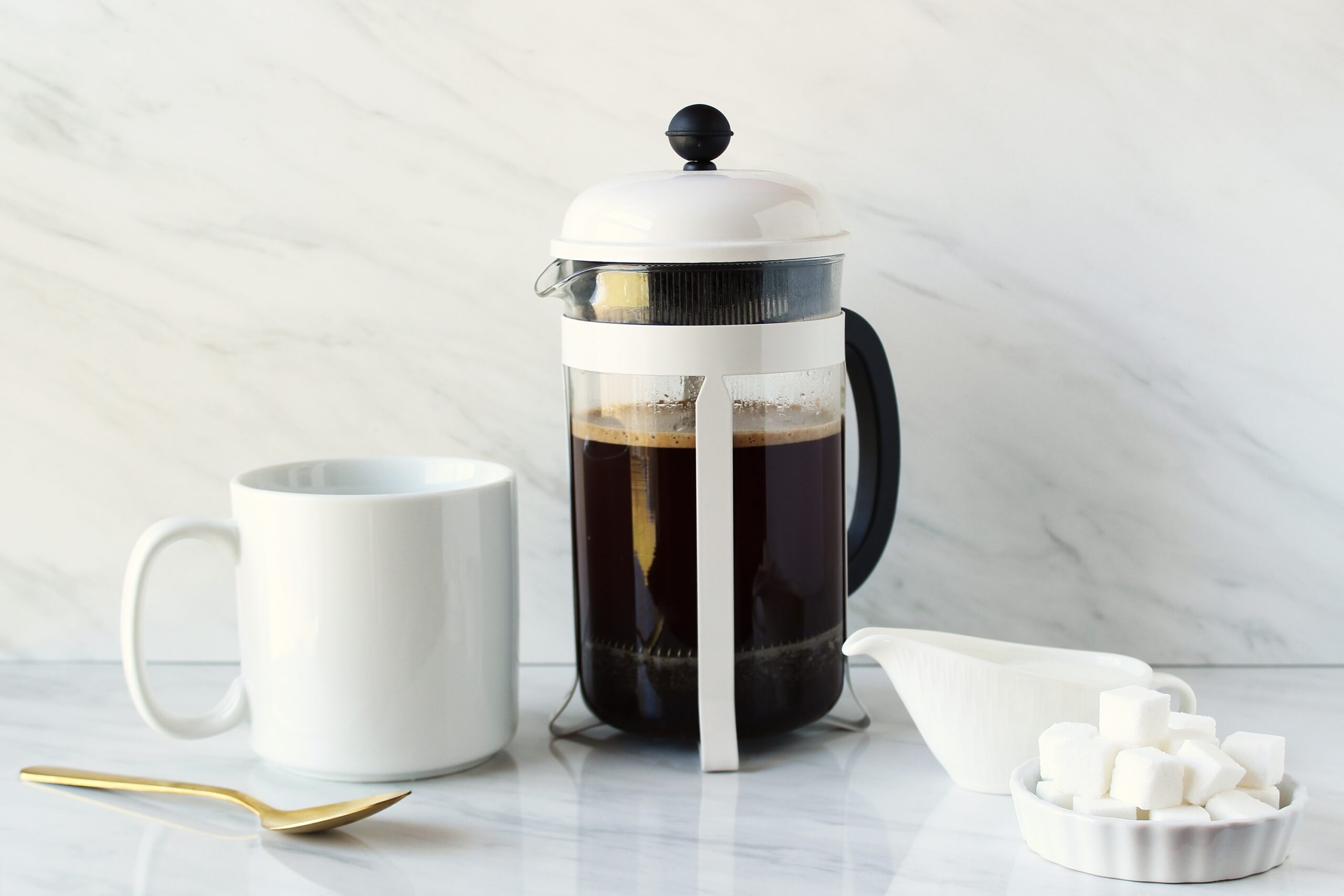A white French press on a counter next to a white coffee mug.