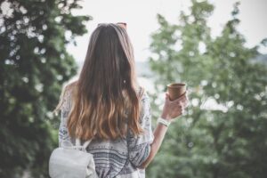 A girl with a backpack holding a cup of coffee.