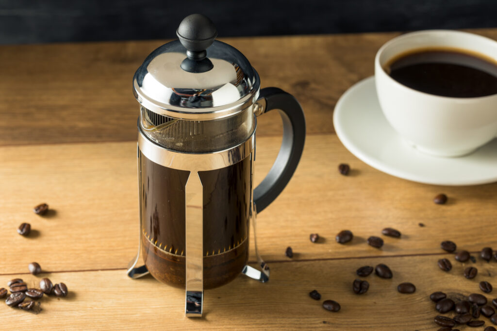 A French press full of coffee on a table next to a coffee cup.