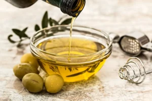A bowl of olive oil surrounded by olives and olive branches.